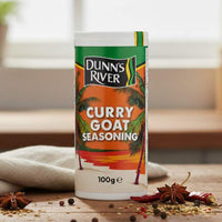 Dunn's River Curry Goat Seasoning container on a wooden surface with spices.