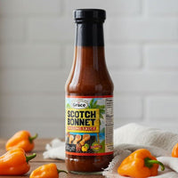 Bottle of Grace Scotch Bonnet Grilling Sauce 340g with Scotch bonnet peppers on a wooden table.