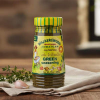Bottle of Walkerswood Jamaican seasoning on a wooden surface with herbs and garlic.