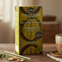 Acan Moringa tea box with a steaming cup of tea on a wooden table.