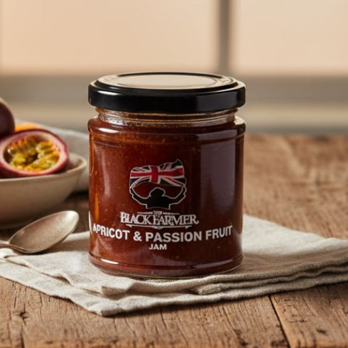 Jar of apricot and passion fruit jam on a wooden table with fruits in the background