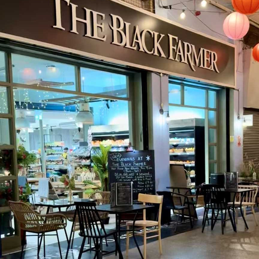 Restaurant entrance with 'The Black Farmer' sign, tables, and chairs inside.