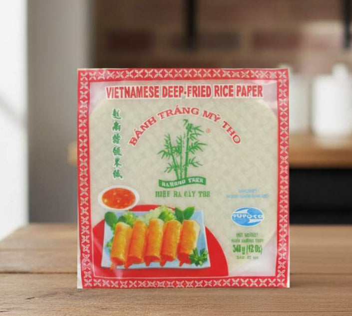 Bamboo Tree Vietnamese Rice Paper 22cm pack on a kitchen table beside herbs and vegetables.