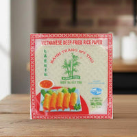 Bamboo Tree Vietnamese Rice Paper 22cm pack on a kitchen table beside herbs and vegetables.