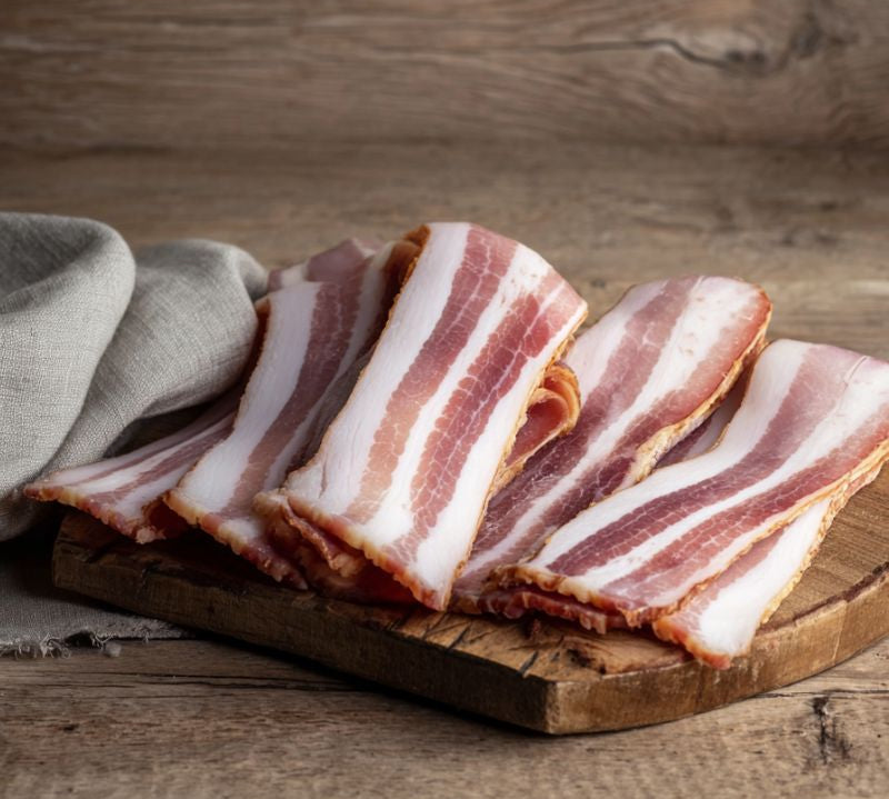 Rind-on smoked streaky bacon rashers on a rustic wooden board — naturally beechwood smoked British pork from The Black Farmer.