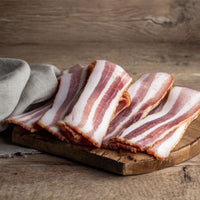 Rind-on smoked streaky bacon rashers on a rustic wooden board — naturally beechwood smoked British pork from The Black Farmer.
