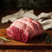 Raw beef on a wooden cutting board with herbs and a cloth in the background
