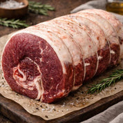 Raw beef brisket on a wooden cutting board with a cloth and tomatoes in the background