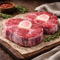 Two raw Beef shin medallions on a wooden cutting board with a cloth in the background
