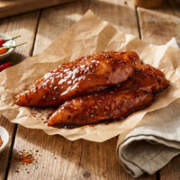 Raw chicken breasts seasoned with spices on a wooden board with herbs and tomatoes.