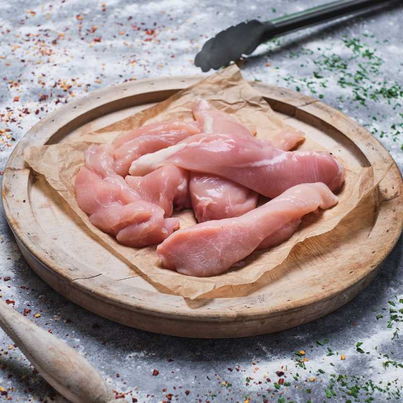 Raw chicken pieces on a wooden cutting board with spices and a wooden spoon in the background.