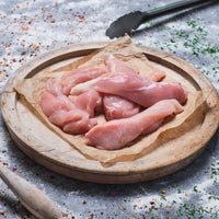 Raw chicken pieces on a wooden cutting board with spices and a wooden spoon in the background.