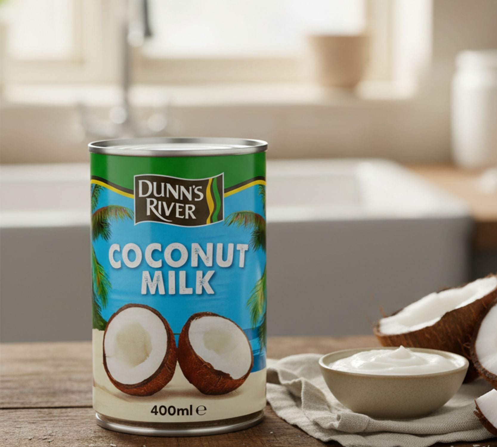 Can of Dunn's River coconut milk on a wooden table with coconuts and a bowl of coconut cream.