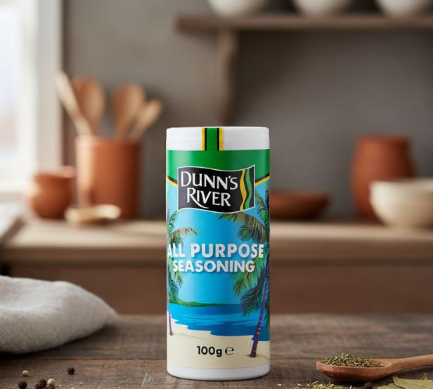 Dunn’s River All Purpose Seasoning 100g — Caribbean spice blend in shaker on kitchen table beside herbs and salt.