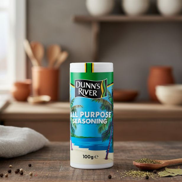Dunn’s River All Purpose Seasoning 100g — Caribbean spice blend in shaker on kitchen table beside herbs and salt.