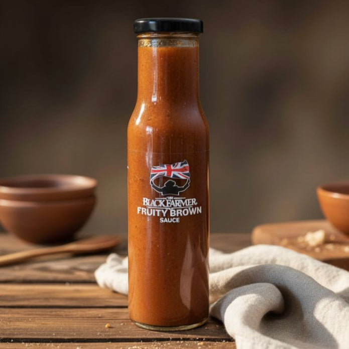 Bottle of Black Farmer Fruity Brown Sauce on a wooden table with bowls in the background