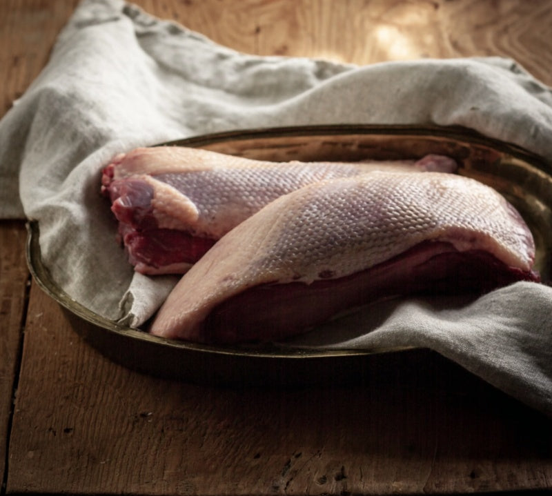 Uncooked British goose breast on a rustic wooden board, seasoned with salt, pepper, and rosemary — premium poultry from The Black Farmer.