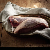 Uncooked British goose breast on a rustic wooden board, seasoned with salt, pepper, and rosemary — premium poultry from The Black Farmer.