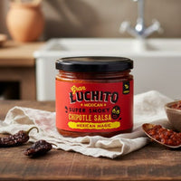 Jar of Gran Luchito chipotle salsa on a kitchen counter with a bowl and spoon.
