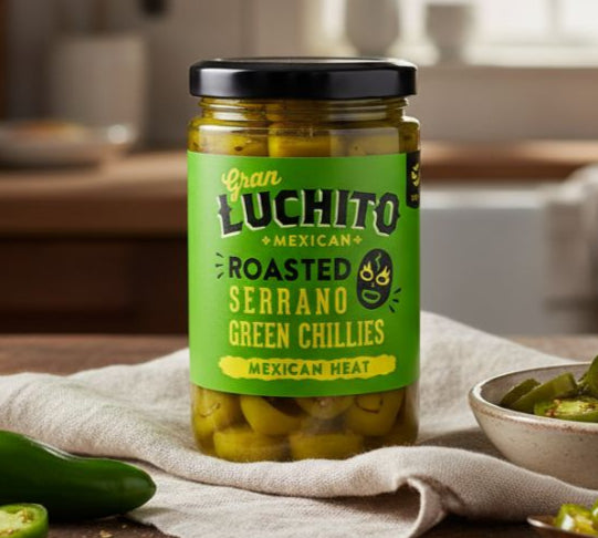 Jar of Juan Luchito roasted serrano green chillies on a wooden table with a kitchen background.