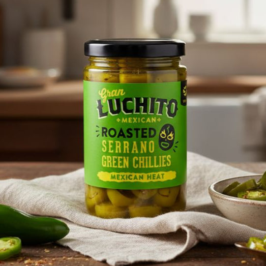 Jar of Juan Luchito roasted serrano green chillies on a wooden table with a kitchen background.