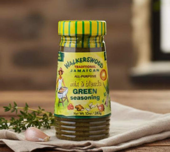 Bottle of Walkerswood Jamaican seasoning on a wooden surface with herbs and garlic.