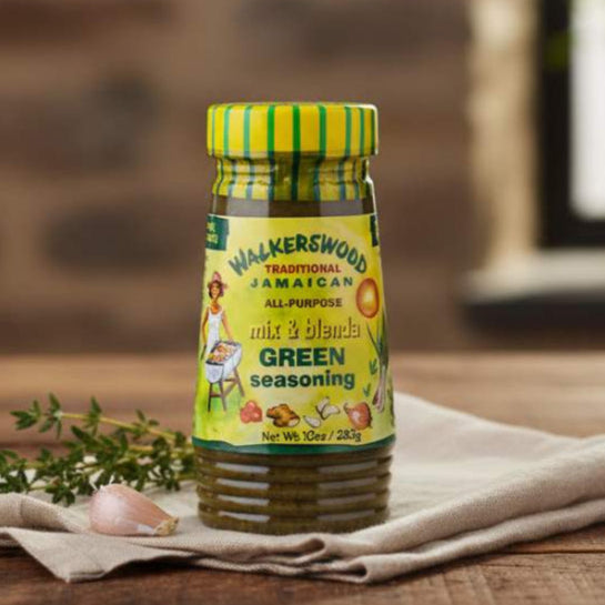 Bottle of Walkerswood Jamaican seasoning on a wooden surface with herbs and garlic.