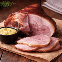 A succulent smoked ham hock, sliced and accompanied by a bowl of mustard, displayed on a wooden board for a rustic touch.