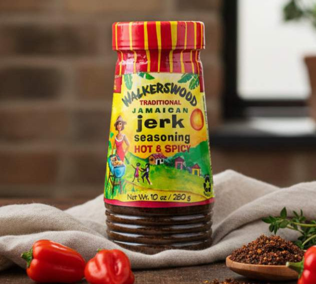 Walkerswood Jamaican jerk seasoning bottle on a wooden surface with peppers and herbs.