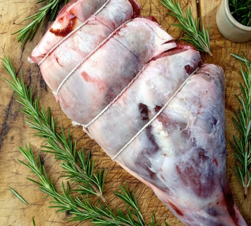 Raw meat with string on a wooden cutting board with rosemary sprigs