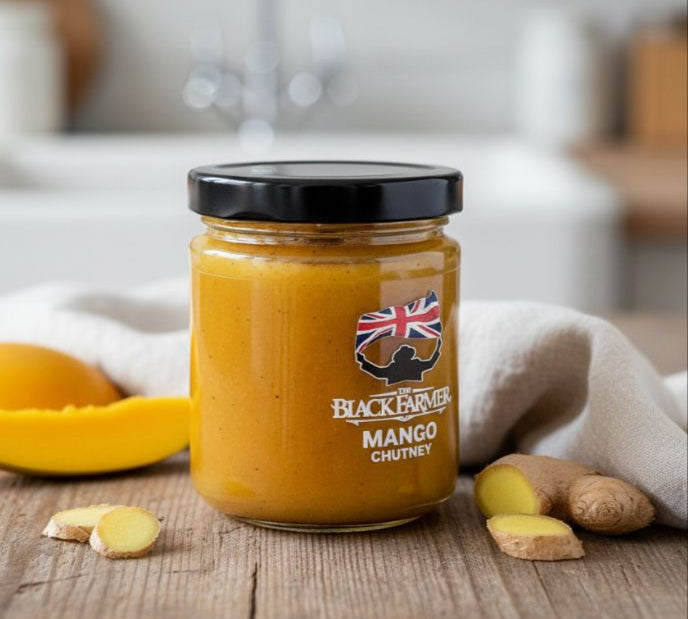 Jar of Blackadder Mango Chutney on a wooden surface with mangoes and ginger.