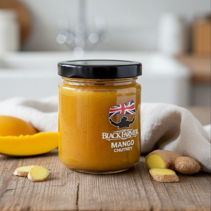 Jar of Blackadder Mango Chutney on a wooden surface with mangoes and ginger.
