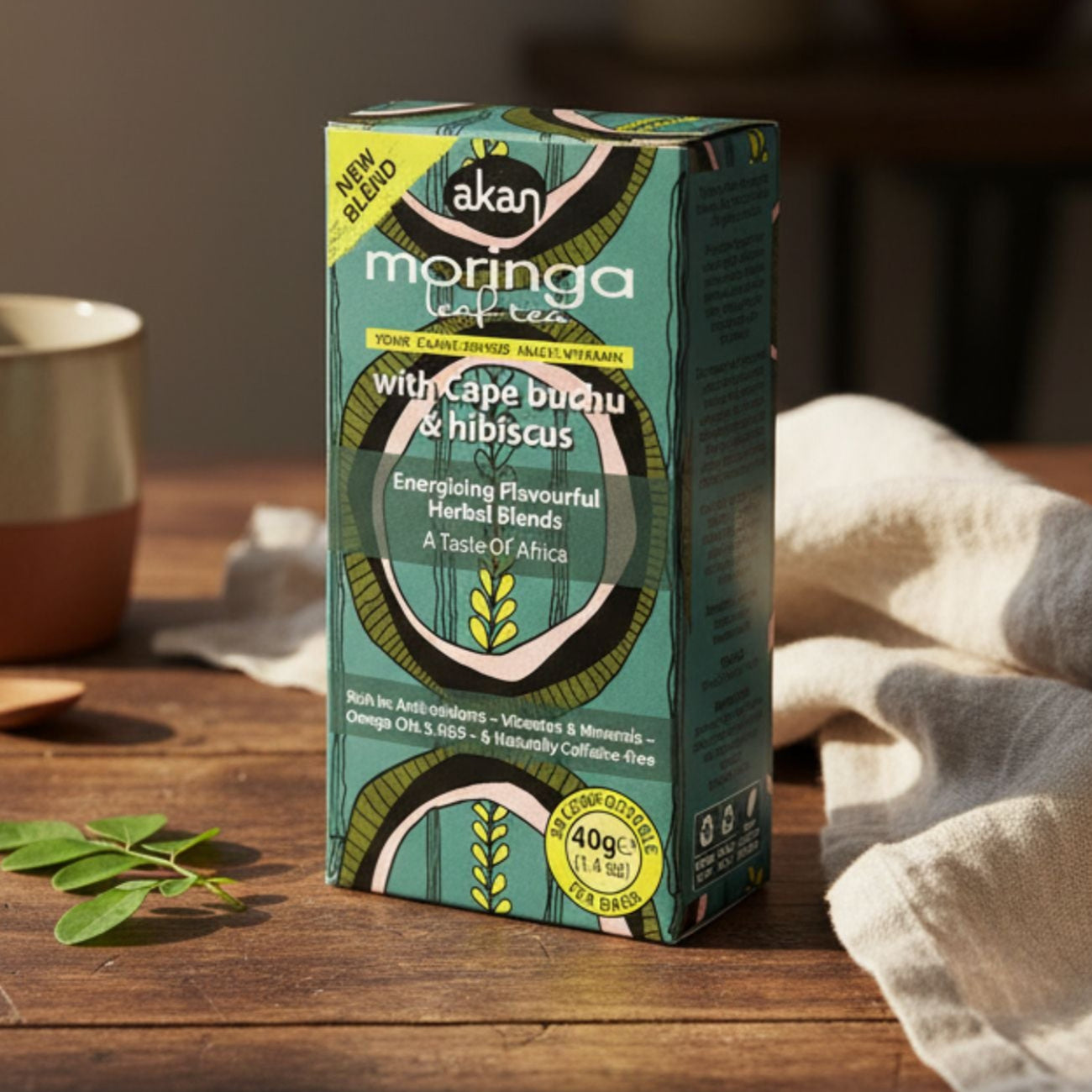 Box of Akan Moringa Coffee on a wooden table with a cup and leaves in the background