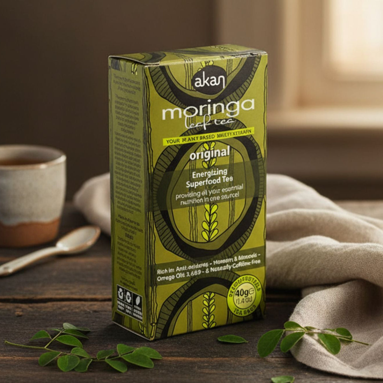 Box of Akan Moringa Superfood Tea on a wooden table with a cup and leaves.