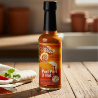 Peri Peri X Hot sauce bottle on a wooden table with ingredients in the background
