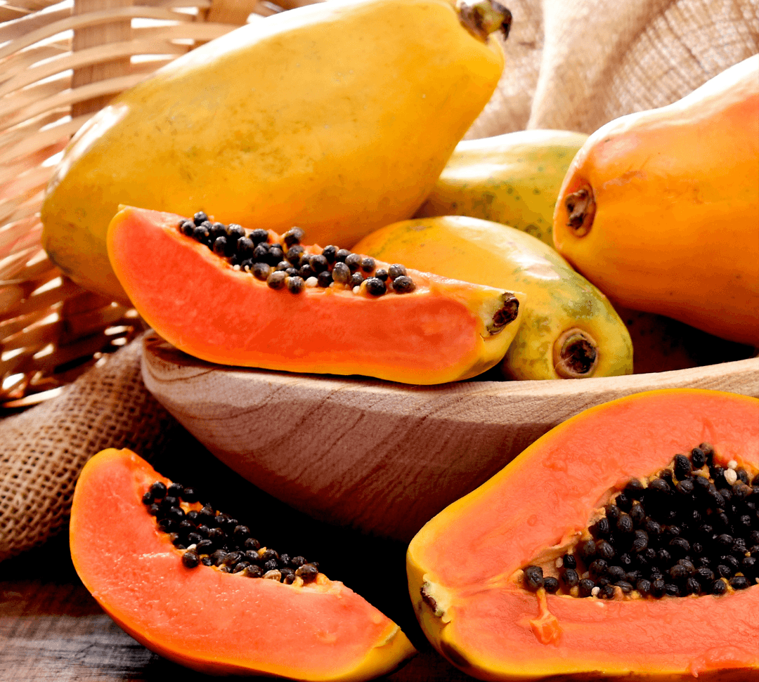 Papayas with a focus on a halved papaya on a wooden surface.