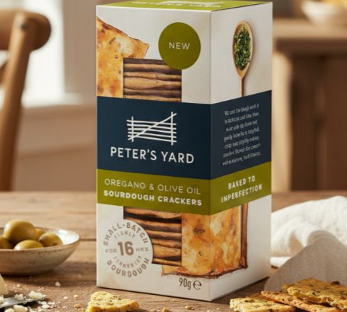 Box of Peter's Yard crackers on a wooden table with crackers and cheese.