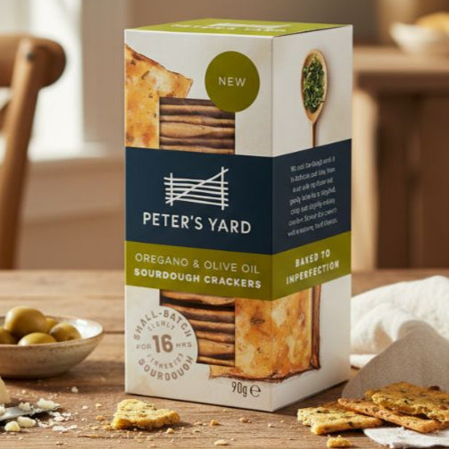 Box of Peter's Yard crackers on a wooden table with crackers and cheese.