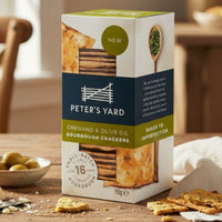 Box of Peter's Yard crackers on a wooden table with crackers and cheese.