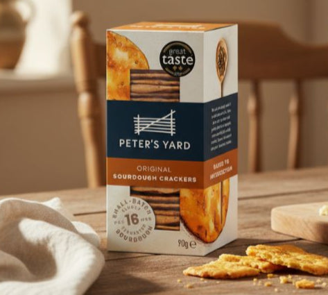 Box of Peter's Yard crackers on a wooden table with crackers and cheese.