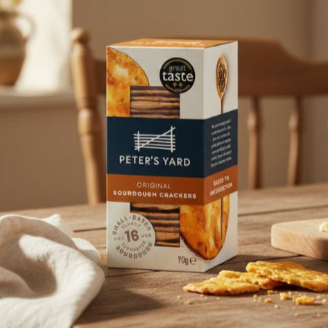Box of Peter's Yard crackers on a wooden table with crackers and cheese.