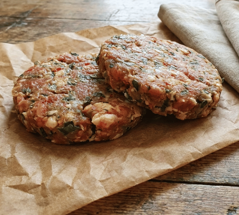 Raw pork, leek and chilli burger patties on a board with leeks and red chilli – The Black Farmer.