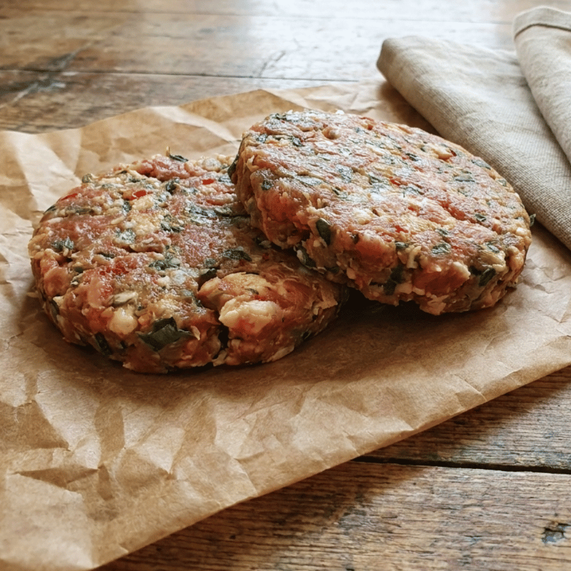Raw pork, leek and chilli burger patties on a board with leeks and red chilli – The Black Farmer.