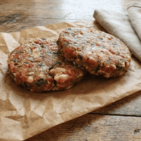 Raw pork, leek and chilli burger patties on a board with leeks and red chilli – The Black Farmer.
