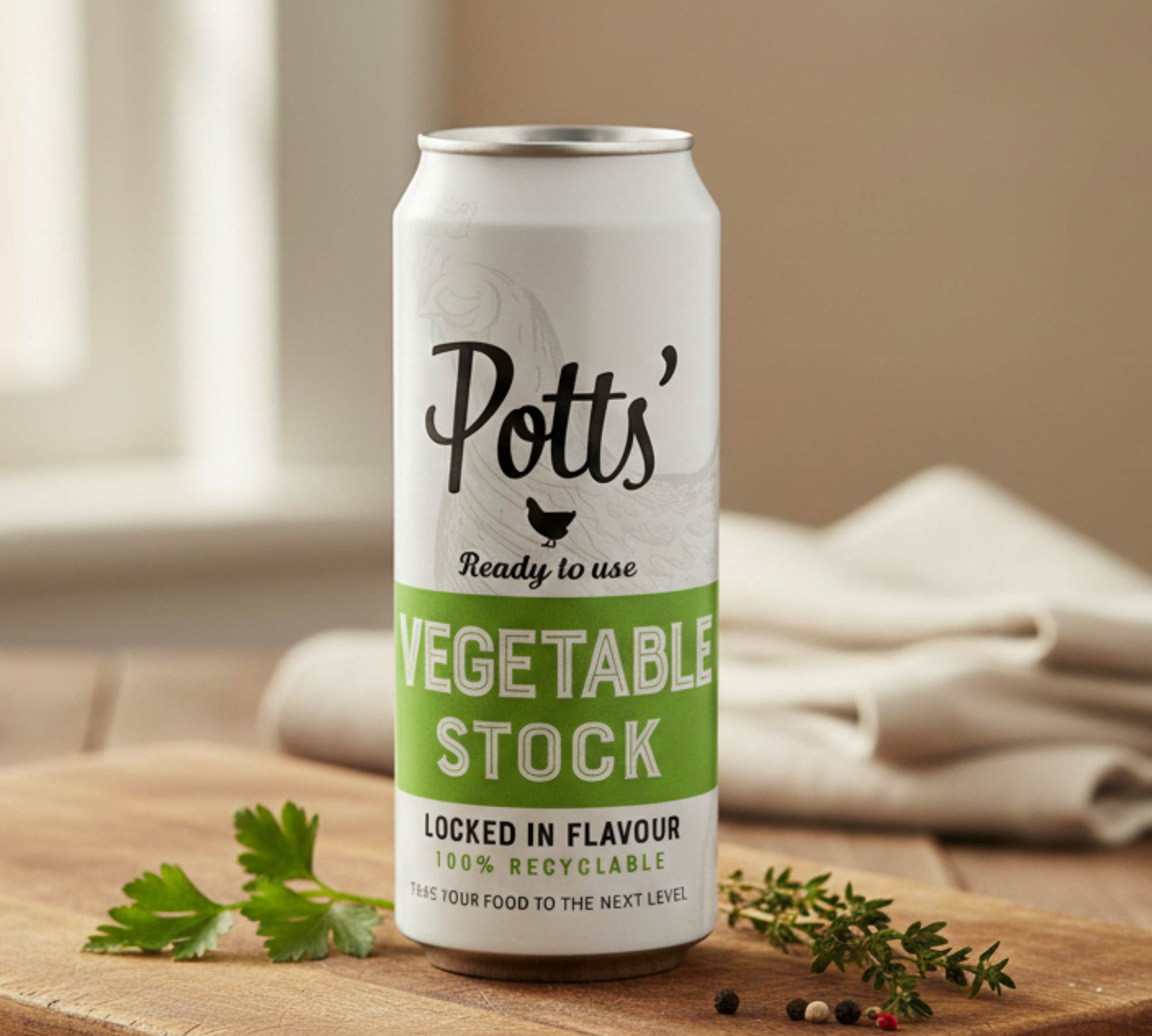 Potts' vegetable stock can on a wooden surface with herbs and a cloth in the background