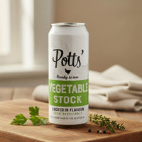 Potts' vegetable stock can on a wooden surface with herbs and a cloth in the background