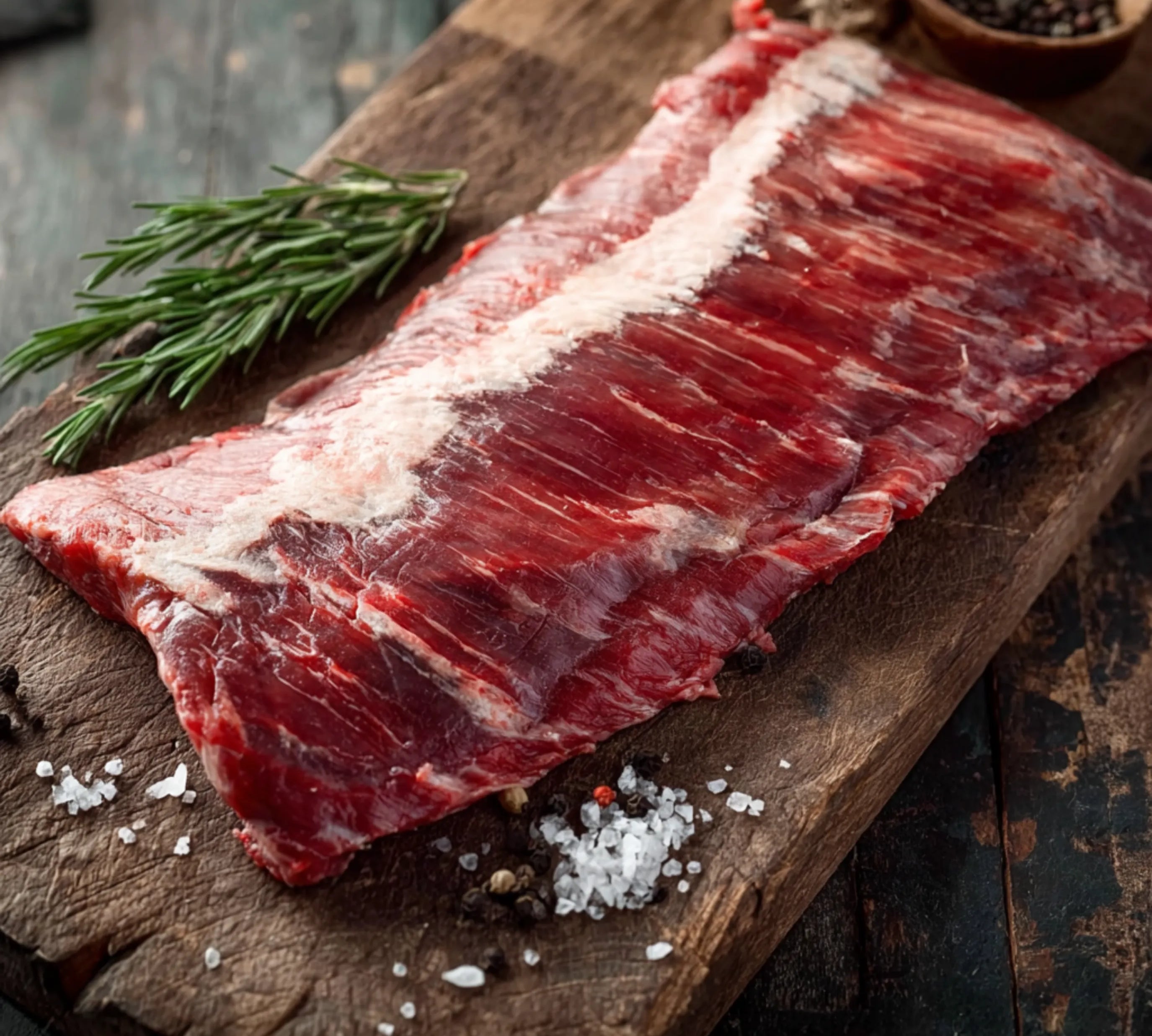 Raw meat on a wooden cutting board with rosemary and salt