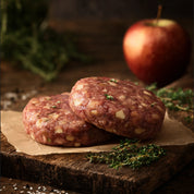 Two raw wild boar and apple burger patties on parchment with fresh apple and herbs – The Black Farmer.