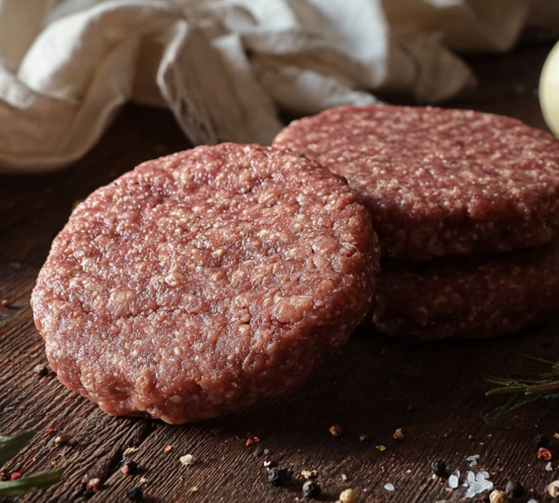 Two raw jerk-seasoned goat burger patties on a board with spices, garlic and herbs – The Black Farmer.