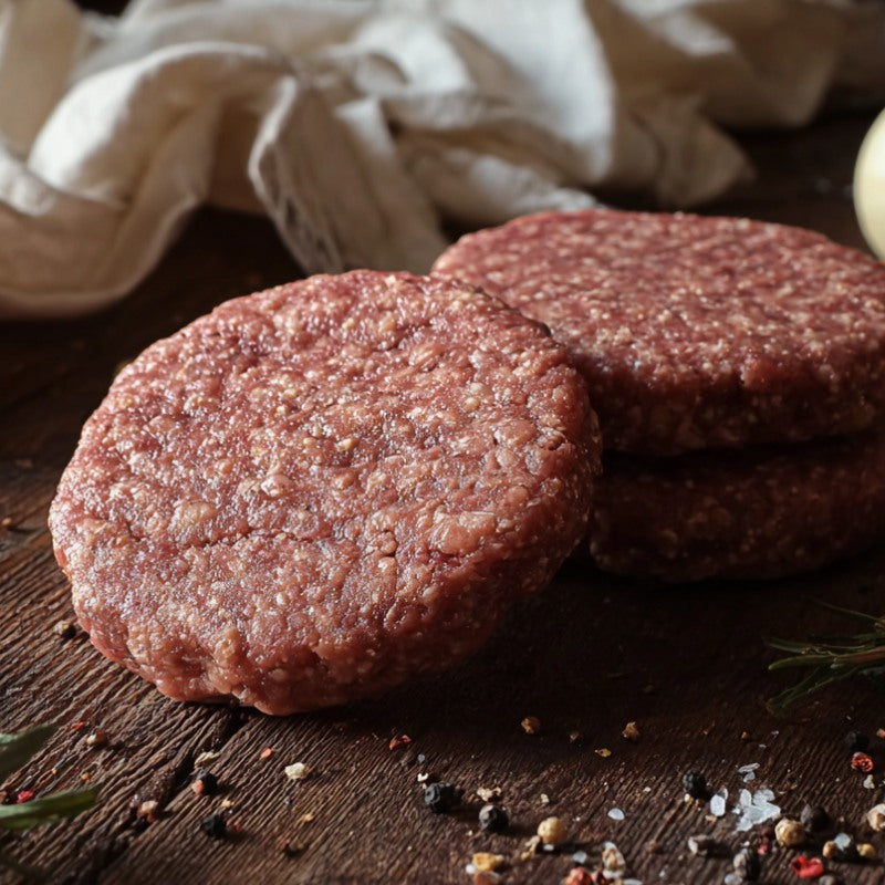 Two raw jerk-seasoned goat burger patties on a board with spices, garlic and herbs – The Black Farmer.
